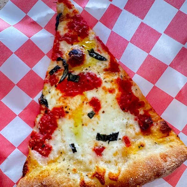 A slice of pizza with red sauce, melted white cheese, and basil on checkered paper.