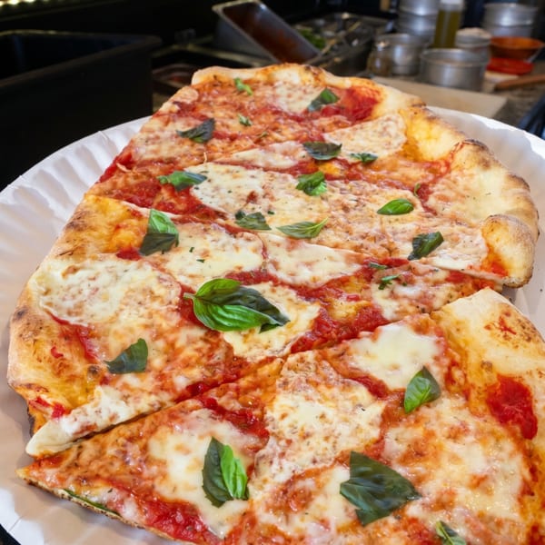 A large, rectangular Margherita pizza with fresh basil leaves on a white paper plate.