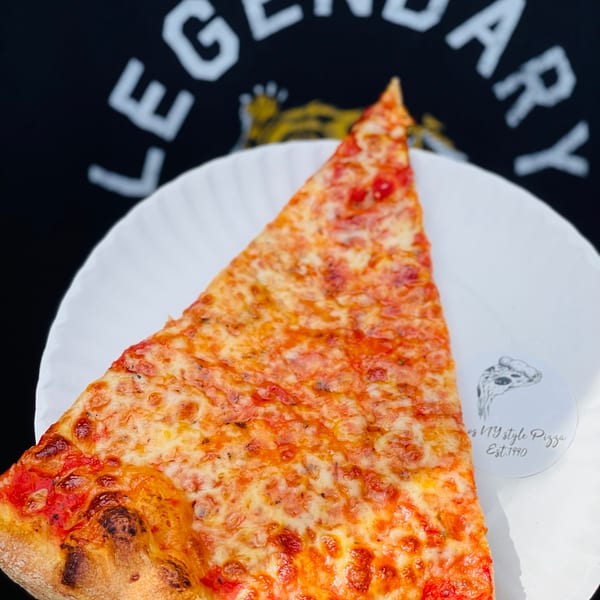A hand in a black glove holds a cheesy pizza slice on a white plate, with a "Legendary" shirt in the background.