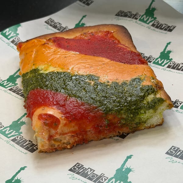 A thick slice of Gino's NY Style pizza with red sauce, orange cheese, and green pesto stripes.