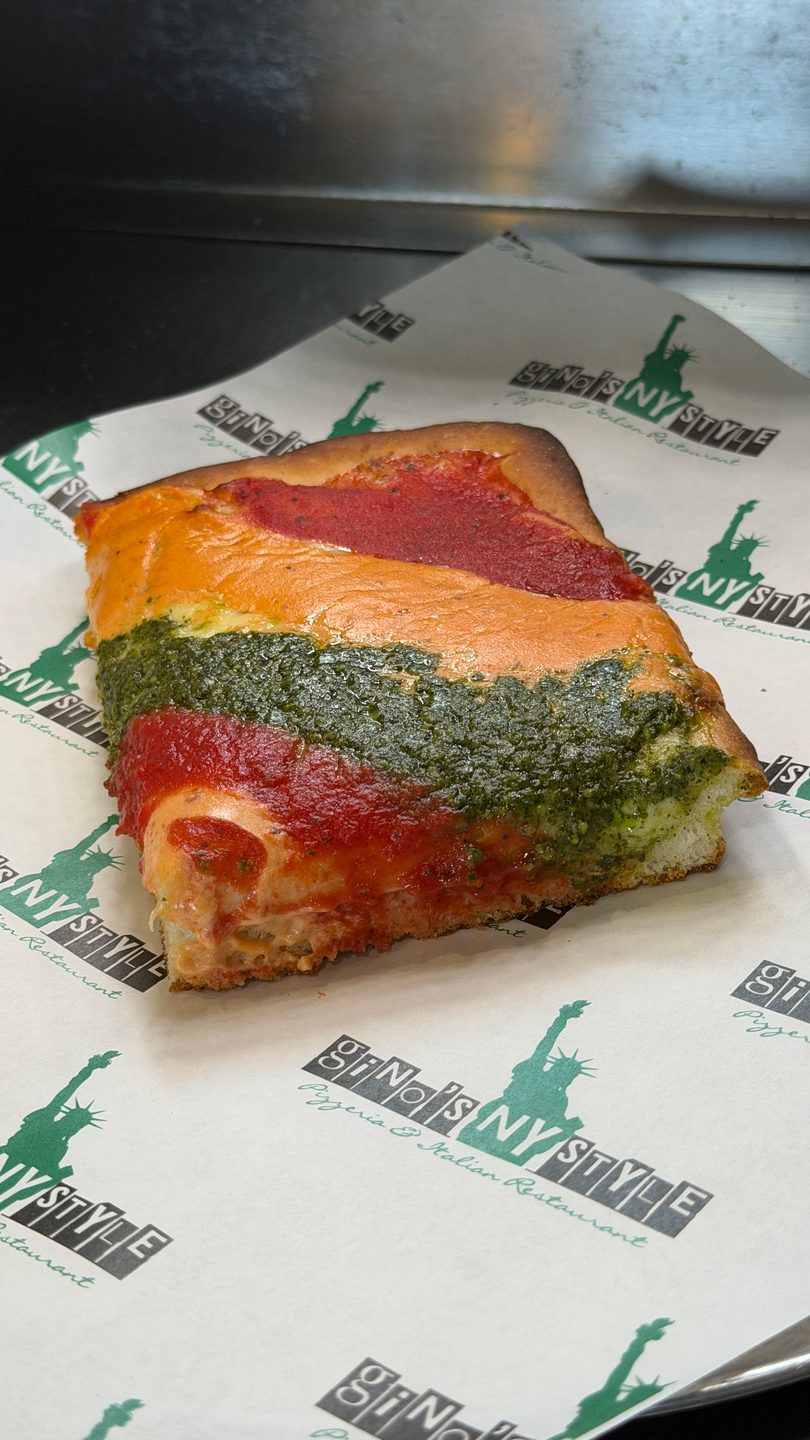A thick slice of Gino's NY Style pizza with stripes of red sauce, orange cheese, and green pesto.
