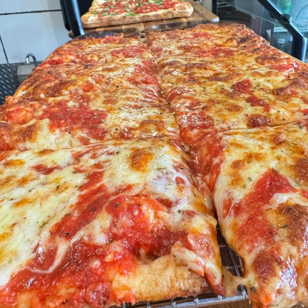 Two large rectangular pizzas with melted cheese and red sauce, one in the foreground, one in the background.