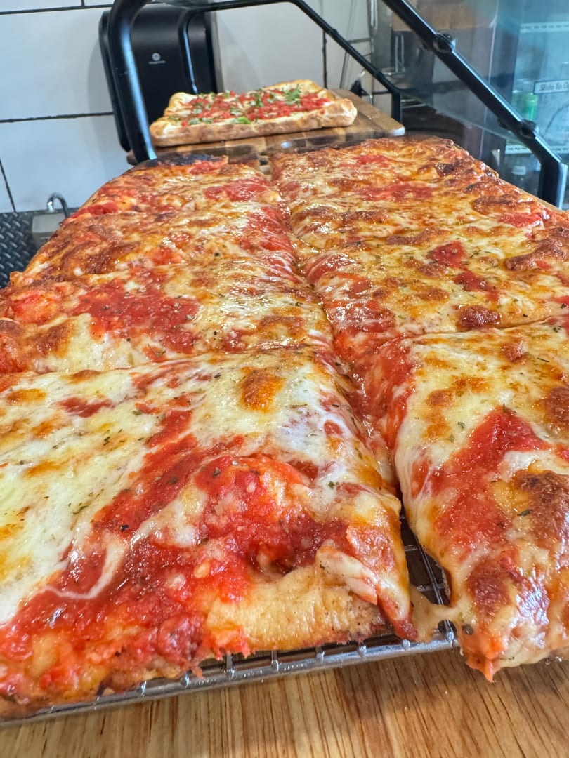 Two large rectangular pizzas with melted cheese and red sauce, one in the foreground, one in the background.