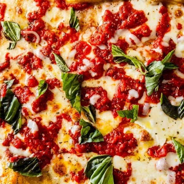 Close-up of a rectangular pizza with melted mozzarella, dollops of red sauce, and fresh basil leaves.