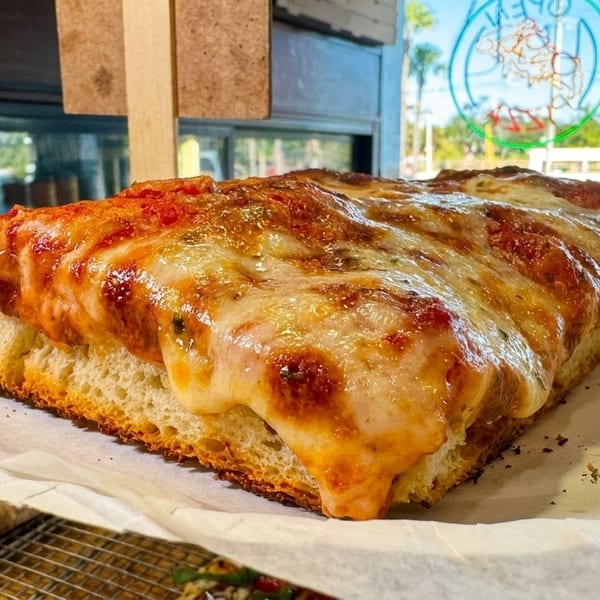 Thick-crust Sicilian pizza slice with melted cheese and tomato sauce on parchment paper.