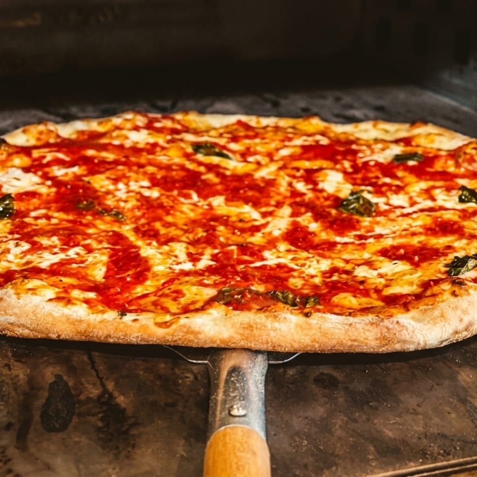 Freshly baked Margherita pizza with basil and mozzarella, being removed from a hot oven.